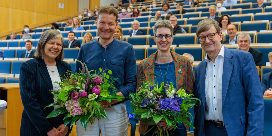 Four people stand in the lecture hall with their backs to the audience. Niels Hovius and Susanne Buiter hold their bouquets.