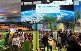 Large screen with Agrisens lettering and a satellite, hung in a hall at the "Grüne Woche" agricultural trade fair.