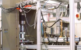 Scene in the geomechanical high-pressure laboratory: metal frame with metal containers, cables, measuring instruments and a press.