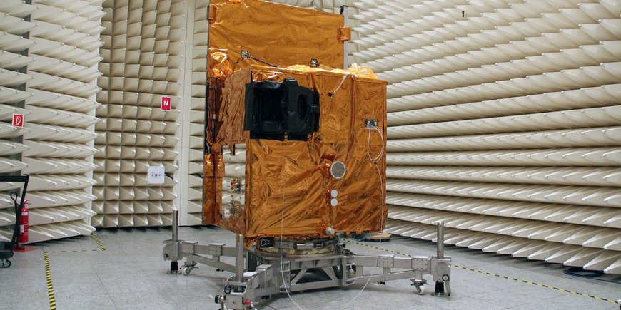 Der kastenförmige EnMAP-Satellit steht in goldener Folie in einem raum mit grauen, schallisolierenden Wänden und wird getestet.