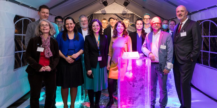 Gruppenfoto der Gäste und Beteiligten aus Politik, Wirtschaft und Wissenschaft vor der Eisblockinstallation.