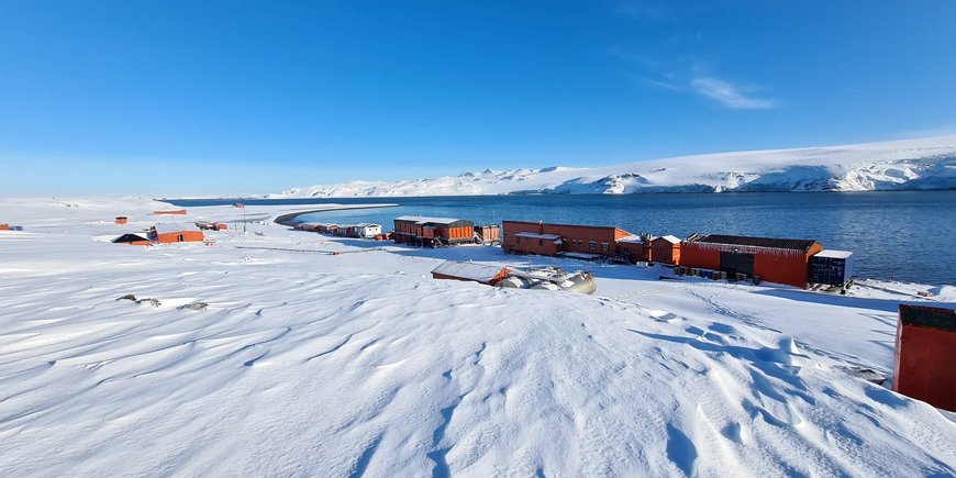 Antarktische Schnee- und Eislandschaft an einer Wasserstraße und mit roten Häusern einer Forschungsstation