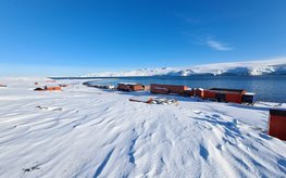 Antarctic snow and ice landscape along a waterway and with red houses of a research station