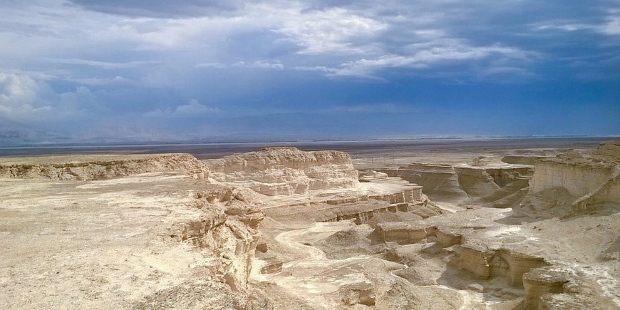 Barren canyon with layered sediment structure, the Dead Sea in the background.
