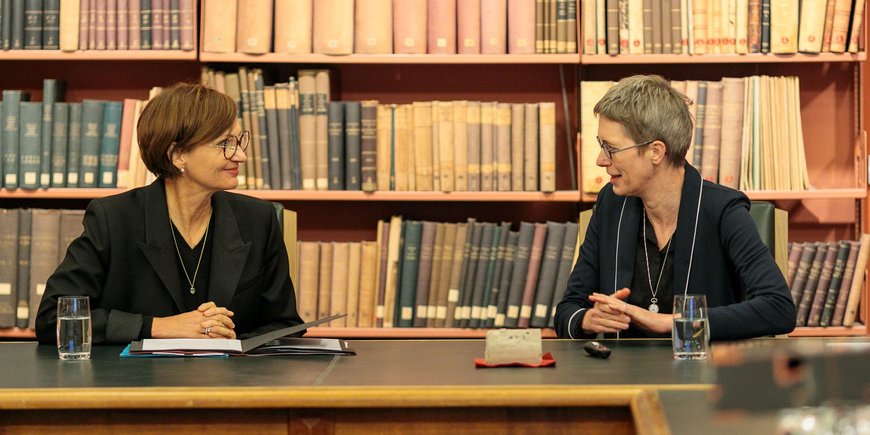 Two women sitting and talking in front of a book shelf in the hitoric library.