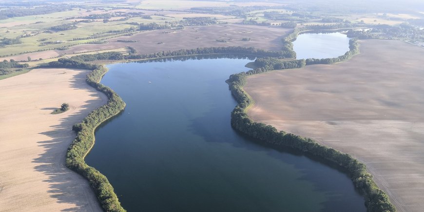 Luftaufnahme des länglichen Sees im flachen Land.