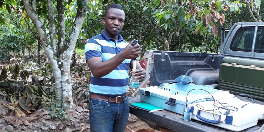 Evans Manu stands by his pickup truck holding lab equipment.