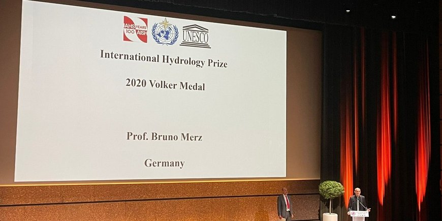 Screen showing the name of the price winner Bruno Merz. Merz speaking to the audience