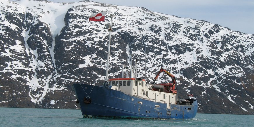 Schiff auf dem Meer, im Hintergrund die Fels- und Eislandschaft von Gröndland.