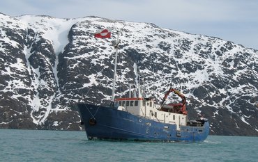Ship at sea, with the rocky and icy landscape of Greenland in the background.