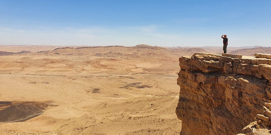 A person stands on a rocky outcrop and looks out into vast desolate land.