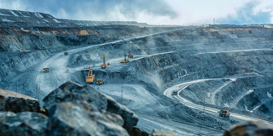 An open pit mine: grey rock, ramps, huge truck loaders driving on them.