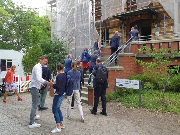 A group of about 20 people walk up the stairs to a scaffolded building.