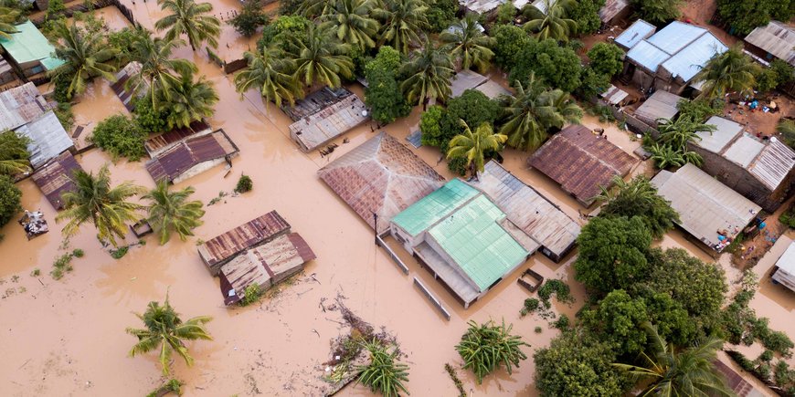 Hellbraunes Hochwasser überflutet kleine Häuser und Palmen.