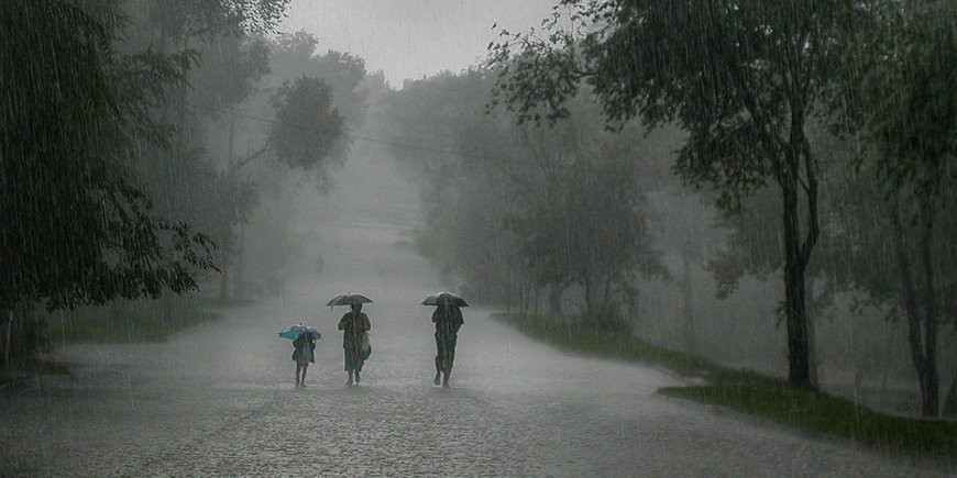 Drei Persoenen mit Regenschirm bei einem heftigen Regen.