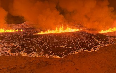 Volcanic eruption from close up: a kind of "lake" of liquid lava, with fire and clouds of smoke, all bathed in orange light