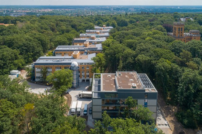 Ein würfelförmiger Neubau im Vordergrund, dahinter eine Reihe weiterer moderner Bauten, alles umgeben von dem Wald auf dem Potsdamer Telegrafenberg.