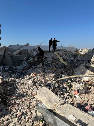 Two people standing on a pile of rubble from collapsed houses.