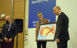 Eine Frau und ein Mann stehen auf einer Bühne und halten gemeinsem ein Bild mit einer eingefärbten Landkarte der Türkei.
