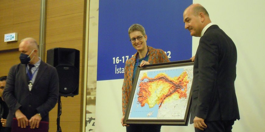 Eine Frau und ein Mann stehen auf einer Bühne und halten gemeinsem ein Bild mit einer eingefärbten Landkarte der Türkei.