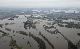 Bild aus dem Flugzeug von einer platten Landschaft, die großflächig überflutet ist: Felder, Straßen und Teile von Ortschaften stehen unter Wasser.