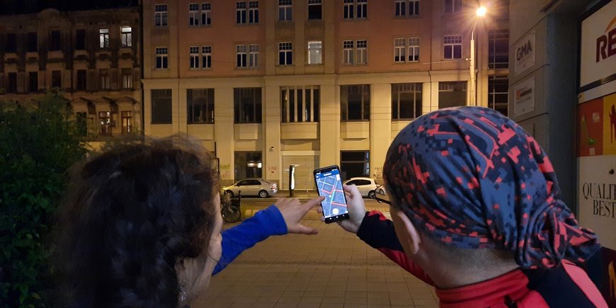 Zwei Menschen stehen nachts in einer Straße und halten ein Smartphone vor sich, um die Beleuchtung mit einer App zu registrieren.