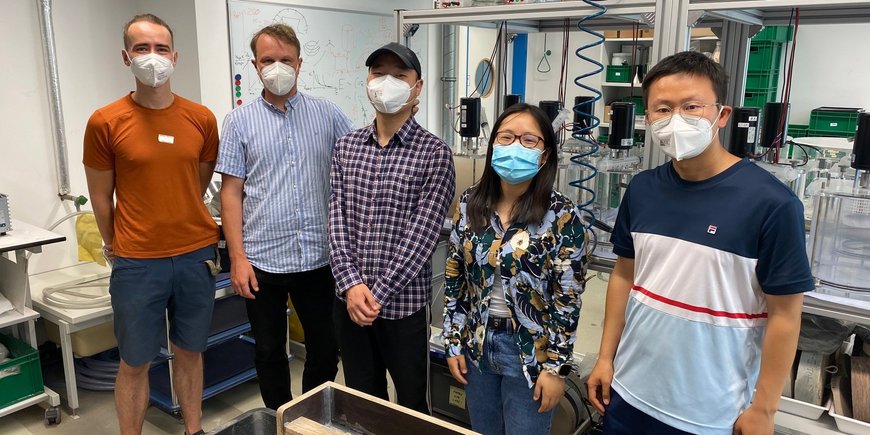 5 people standing in a laboratory wearing a mask.
