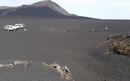 Two white off-road vehicles are parked on a grey scoria field on the volcano Etna and four people are digging the trench for the fibre optic cable with shovels.