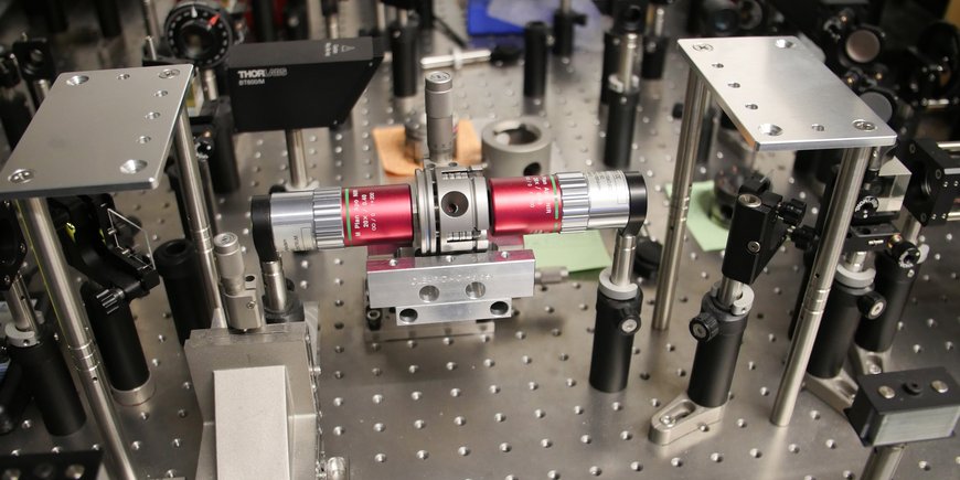 A laser table in the laboratory: many lenses and other optical elements are screwed onto a metal plate. In the centre is the palm-sized metal diamond anvil cell.