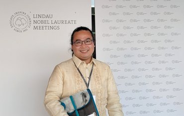 Jeffrey Perez in front of the Logo of the meeting