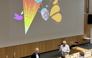 Lecture hall, Onno Oncken and Friedhelm von Blanckenburg are standing in the front, one can see some audience from backwards, at the screen a figure with the lithosphere and F.v.B. as butterfly