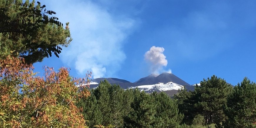 small ash cloud over the volcano Etna from a distance, in front of it forest/greenery