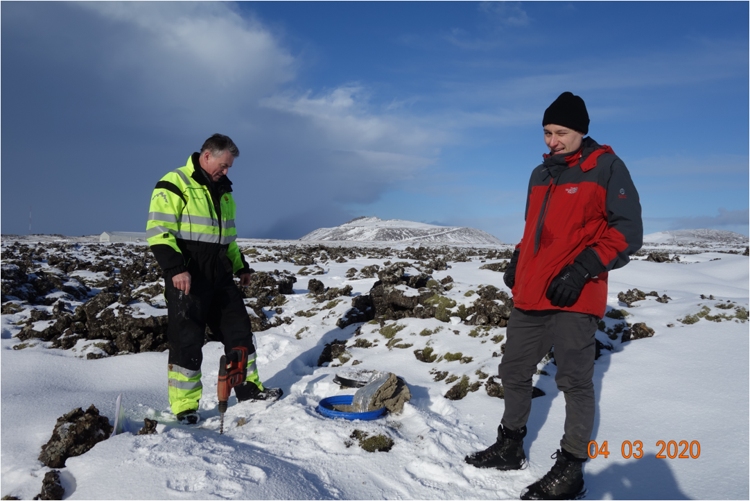 Zwei Menschen stehen im Schnee an einem Loch, wo das Messgerät eingelassen wird.